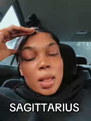 A close-up shot of a woman inside a car, possibly in a selfie, with closed eyes appearing to be speaking or singing, and the word "SAGITTARIUS" is at the bottom. The background is blurred, showing a window and perhaps some trees. The car's interior is dark, with a focus on the woman's face.