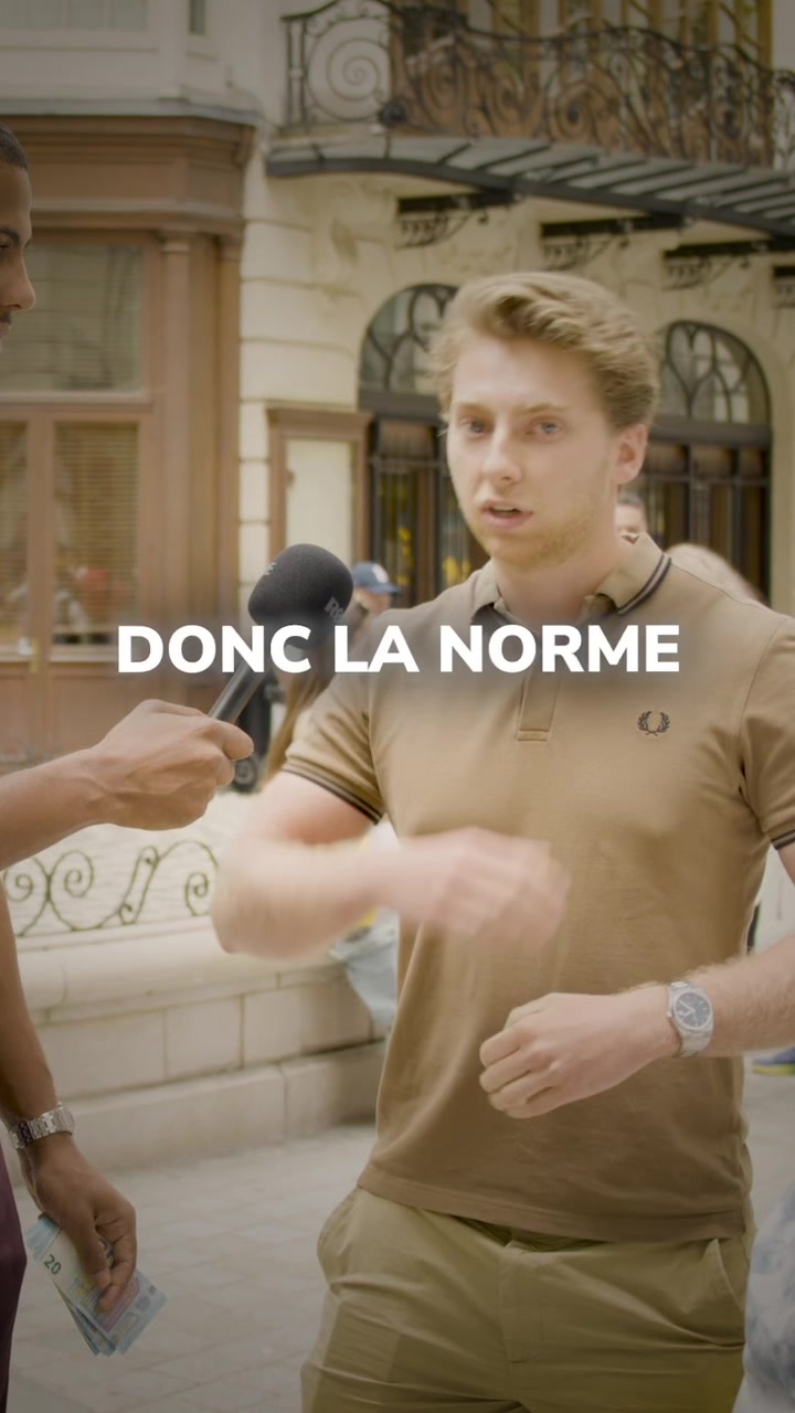 A man is being interviewed on the street. He's wearing a tan polo shirt and khaki pants, and has a watch. Another person is holding a microphone up to him. Text on the screen reads, "DONC LA NORME."