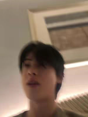 The image shows a blurry, close-up shot of a man's face. The lighting appears soft, and the background gives a sense of being indoors. The man seems to be looking down, possibly speaking, as his mouth is slightly open.