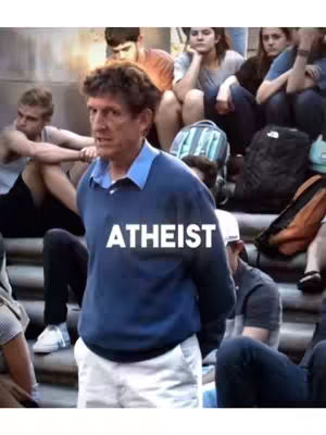A man in a blue sweater stands in front of a crowd of students, with the word 'ATHEIST' in white letters superimposed over his chest.