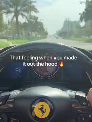 An interior shot of a car's dashboard with the steering wheel in the foreground. On the dashboard, the car's gauges and speedometer are visible, along with a digital display. The steering wheel features a Ferrari emblem at its center. Through the front windshield, the road ahead is slightly blurred, suggesting movement. Text overlays are superimposed at the top and bottom of the dashboard.