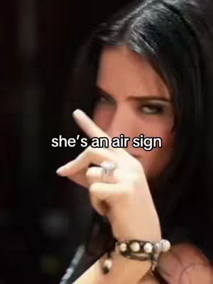 A medium shot features a woman with dark hair and eyes. She's pointing with her right hand with a peace-sign style gesture and her left hand is covering part of her face. Overlayed text indicates a focus on zodiac signs.