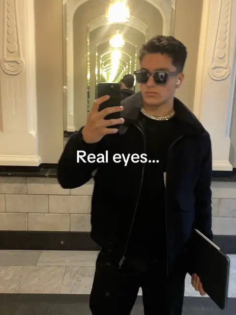 A man in sunglasses is taking a selfie in a hallway with mirrors on both sides, creating an infinity effect. He is wearing a black jacket and holding a phone, with text overlayed.