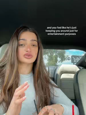 A young woman is sitting inside a car, looking towards the camera and talking, while gesturing with her hands. Text overlayed on the image reads, "and you feel like he's just keeping you around just for entertainment purposes."