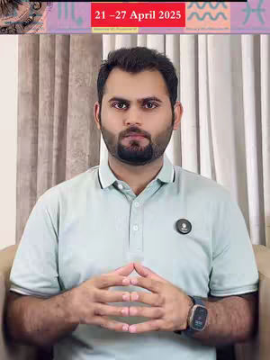 A man with a beard is centered in the frame, wearing a light green polo shirt. Behind him are beige curtains. Above the man, a banner reads '21-27 April 2025'. The man's hands are clasped in front of him, and he wears a watch on his left wrist. The overall composition is simple, focusing on the man as the central subject.