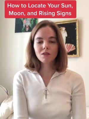 A woman is centered in front of a neutral background, with text overlayed at the top of the image which is in a bright red rectangle. The woman has light brown hair, is wearing a white top, and appears to be speaking. Behind her are two pieces of wall decor.