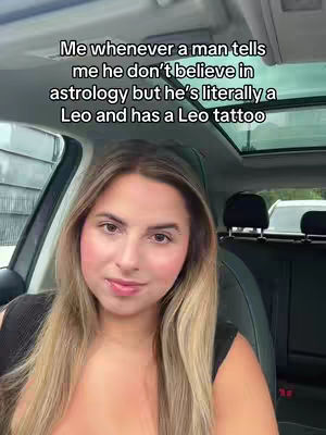 A woman is filmed from the chest up inside a car, angled slightly from below. She has long blonde hair and is wearing a sleeveless black top. The text overlay says, “Me whenever a man tells me he don’t believe in astrology but he’s literally a Leo and has a Leo tattoo”. The background shows a partially visible car window, black headrest, and the top of the car with a sun roof.