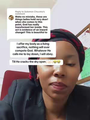 A woman with a head covering, likely a hijab or scarf, is captured in a selfie shot. She is positioned centered in the frame, lit by daylight. On the screen, there are text bubbles that seem to be user-generated comments or speech bubbles, some overlapping her face, others beside her. The background suggests an office or domestic setting, with what seems to be a framed document or artwork visible on the wall behind her. The overall composition is focused on intimate communication or interaction.