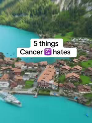 An overhead shot of a village nestled along a turquoise lake, with green mountains in the background. A white rectangle with black text and a purple Cancer symbol is overlaid on the image.