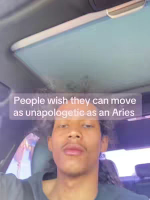 A selfie video taken from inside a car. A young man with curly hair and a mustache is looking at the camera. The text overlay reads: 'People wish they can move as unapologetic as an Aries'. The background includes the sun roof and car interior.
