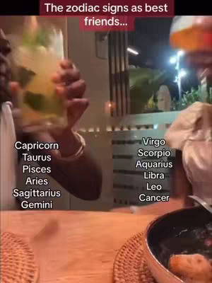 The image captures a dining scene with social interaction, featuring a person holding a cocktail glass. The frame showcases a wooden table laden with several items: a cocktail with a garnish, which the person to the left is holding up in cheers; on the right, there is a partial view of another person. Behind them, the background includes a suggestion of an outside setting. The image uses soft, natural lighting and warm tones.