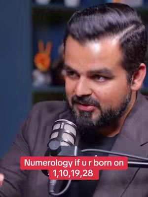 The cover image features a man in a coat speaking into a microphone. A red banner overlaid on the bottom of the image includes the text: "Numerology if u r born on 1,10,19,28". The background includes a blurred shelf.