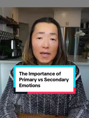 A man with long, dark hair is centered in the frame, looking at the camera and speaking. A rectangular text box with a teal background and black text is overlaid at the bottom of the image. Background elements like a kitchen are slightly visible behind the man, with soft lighting.