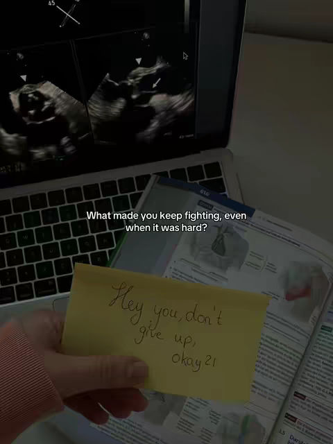 The image shows a hand holding a yellow sticky note with the handwritten message, 'Hey you, don't give up, okay 21,' against a backdrop of a laptop displaying an ultrasound image and a textbook or study guide.