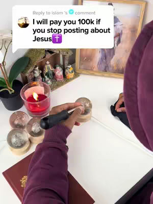 The image displays a close-up of a person's hands working with various objects on a white surface. There's a red candle in a holder to the left, and other glass orbs. A speech bubble graphic is on the upper left corner.