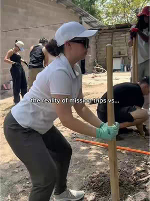 A woman in a white cap, sunglasses, and a white shirt is the main focus, holding a wooden pole, working in what appears to be a construction or outdoor setting. Other people are visible in the background, engaged in similar activities. The text overlay reads: "the reality of mission trips vs..."