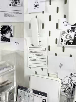 An organized desk with a white pegboard as a backdrop. The pegboard is filled with various small, white paper notes and sketches. A stapler grips a central note. A clear organizer filled with pens and other desk supplies sits in the foreground.