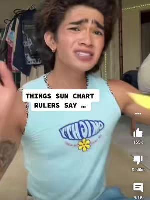 The cover image shows a person of East Asian descent with short, dark hair, making a facial expression with an open mouth and raised eyebrows. The person is wearing a light blue tank top with a design on the front. The background is blurry, but a rack of clothing is visible. The text overlay reads "THINGS SUN CHART RULERS SAY ...".