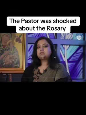 A woman with dark hair and a black shirt sits in front of a window with colorful stained glass. A framed religious painting hangs to the left. Text overlayed at the top reads 'The Pastor was shocked about the Rosary'.