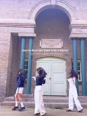 Three young women are captured in motion in front of an old stone building. The women are dancing in front of an arched entrance. Text overlays appear at the top and the bottom of the image.