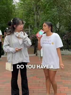 Two young women are standing outside, one holding a phone. Text overlay is positioned at the bottom.