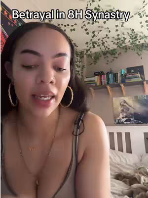 A medium shot showing a woman in a room. She is the central focus, talking to the camera with a serious expression. Overhead, there is greenery. Behind her are shelves filled with books and decorative items. The color palette includes warm tones from the lighting, her skin, and background elements. There is a text overlay at the top.