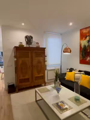 A living room with a wooden cabinet, a white coffee table, a black sofa with yellow pillows and a copper lamp, and an abstract painting.