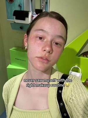 A selfie-style image featuring a young woman in a light green outfit. The background shows a bright green shelf unit and some boxes. The woman is gazing directly at the camera; a text overlay reading, "never saw myself with the right makeup routine" is present at the bottom. The lighting is soft and natural.