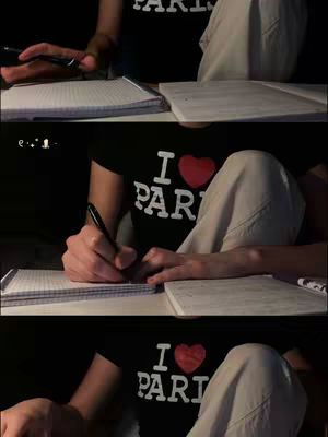 The cover image is a three-panel composite featuring a person, likely the creator. They are wearing a black t-shirt with "I ❤️ PARIS" in white letters and a red heart. They're sitting at what appears to be a desk, writing in a notebook. The lighting is dim, casting shadows, and the shot focuses on the person's hands, the notebook, and bits of their clothing. The background fades into darkness.