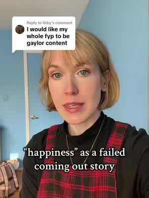 A woman with fair skin and blonde hair stands in front of a light blue wall. She's wearing a black top and a red plaid jumper. A comment is overlaid from Libby, that states 'I would like my whole fyp to be gaylor content.' Text overlayed states, 'happiness' as a failed coming out story.