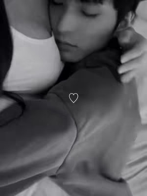 A grayscale image captures a tender moment of a couple hugging, with one person's face nestled against the other's shoulder. The composition is intimate and softly lit, with a simple white heart symbol overlaid.