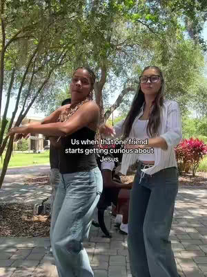 The image shows two young women, presumably friends, dancing and looking energetic outdoors. The background has green trees and what seems like a pathway. There is an overlaid text on the the middle of the image.