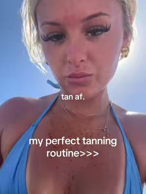 The image shows a close-up of a blonde woman. She is wearing a blue bikini top and a gold necklace. The background is a light blue color. Text overlays on the image say 'tan af.' and 'my perfect tanning routine>>>'.