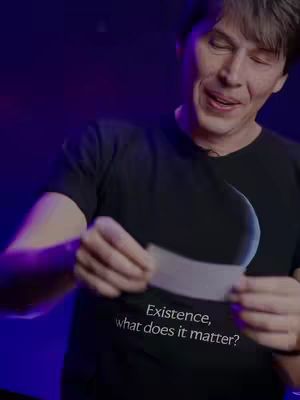 A man with short hair in a black t-shirt holds a curved white piece of paper. The background has purple and blue lighting.