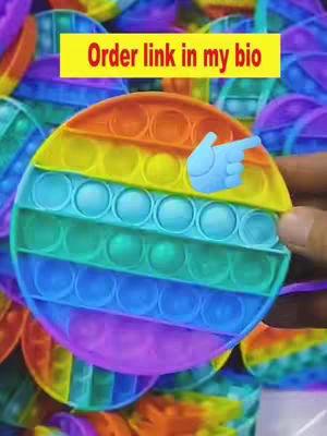 The cover image shows a close-up of a colorful circular pop-it toy. The toy is segmented into rainbow-colored sections and features multiple small, button-like bubbles. A hand is partially visible, holding the pop-it, and a blue pointing finger emoji is overlaid.