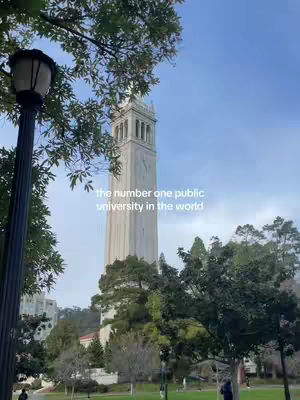 An outdoor shot features a tall, white stone clock tower rising above green trees, set against a blue sky. The image includes a lamp post in the foreground and a person walking on a lower level.