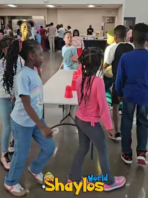 The cover image shows a group of children playing a game with red cups on a table, in a casual setting. The layout includes a table in the middle with red cups and several children walking around it with a few adults in the background. Colors include a red cup with a white table and various colors from the children's clothing.