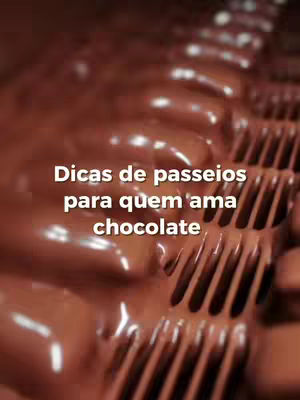The cover image features a close-up view of a flowing, glossy, dark brown substance, resembling melted chocolate. The image has a blurred background focusing on the details of the flowing material. Overlaid centrally on the chocolate is the text 'Dicas de passeios para quem ama chocolate' in white, sans-serif font with a slight blur, to enhance readability.