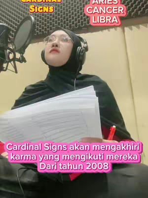 A woman wearing a black hijab and headphones is seated in a recording studio. She is holding a stack of papers and a red pen. Text overlays identify astrological signs.
