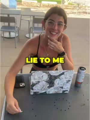 A woman in glasses smiles and touches her chin, sitting at a table with a laptop, phone, and drink, with text overlayed.