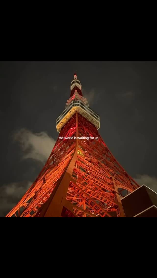 A nighttime shot of the Tokyo Tower. The tower is lit up with glowing red lights, standing tall against a dark, cloudy sky. The image is framed from a low angle. Text is overlaid on the image.