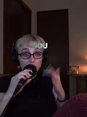 A woman with short blonde hair and glasses is holding a microphone close to her mouth. She is wearing headphones and a black top. The word "YOU" is overlaid on her forehead. The background is dark and indistinct.