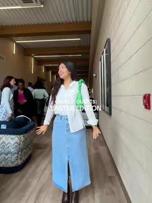 A woman stands in a well-lit hallway, facing the camera with a smile. She's wearing a white top and a long denim skirt with a front slit. She holds a green purse over her shoulder. The background shows other people and architectural details of the building. Text overlayed on the image says 'church outfits: EASTER EDITION'.