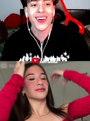 The cover image is a split-screen showing two people. The top half features a young man with short, curly brown hair, wearing a black hoodie with white text on it and white earphones. He is positioned against a blurred, dark background, with a red chair in the background and he appears to be smiling and looking upwards. The bottom half shows a young woman with long dark hair and a red shirt, who is touching her hair with her hands, looking at the camera with a slightly upward gaze.