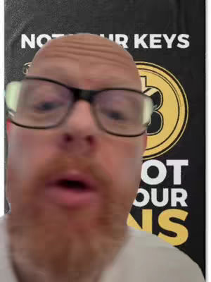 A man with glasses and a red beard is the focus, with text that reads "NOT YOUR KEYS" and an image of a Bitcoin coin. The background is black. The lighting seems to be centered on the man's face.