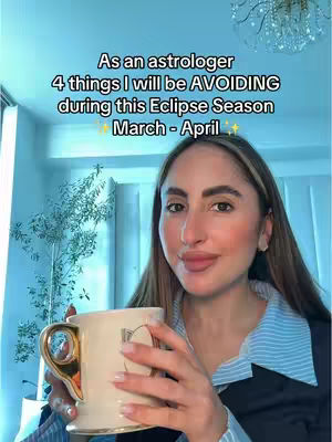 A woman with long brown hair is holding a mug with both hands against the background. The woman has fair skin and is wearing a striped shirt and blazer. Text overlayed at the top says, 'As an astrologer 4 things I will be AVOIDING during this Eclipse Season March-April'. The tones are light, and the setting appears to be indoors.