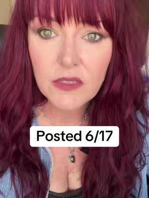 A medium shot of a woman with long, wavy, burgundy hair and fair skin. She has green eyes, light eye makeup, and dark red lipstick. A white rectangular box with the text "Posted 6/17" is overlaid. She's wearing a light blue top. The background is blurred.