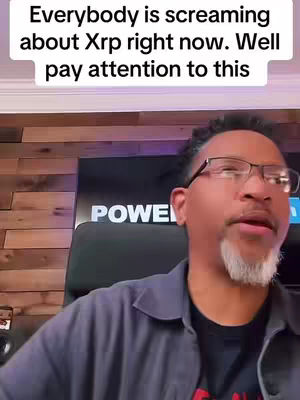 A man in glasses and a grey collared shirt speaks to the camera. Text overlay indicates that the video is about crypto, in front of a wooden wall.