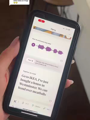 A hand, with manicured nails, holds a smartphone displaying a dating app. The phone's screen showcases a profile with a voice note, and a message about going to IKEA. The background is a blurred, neutral color.