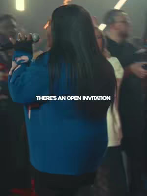 The cover image shows a woman with long dark hair, viewed from the back, singing into a microphone. She is wearing a blue sweatshirt and is positioned in front of a crowd, suggesting a concert or worship service. Text overlayed on the image reads 'THERE'S AN OPEN INVITATION' in white against the darker background.